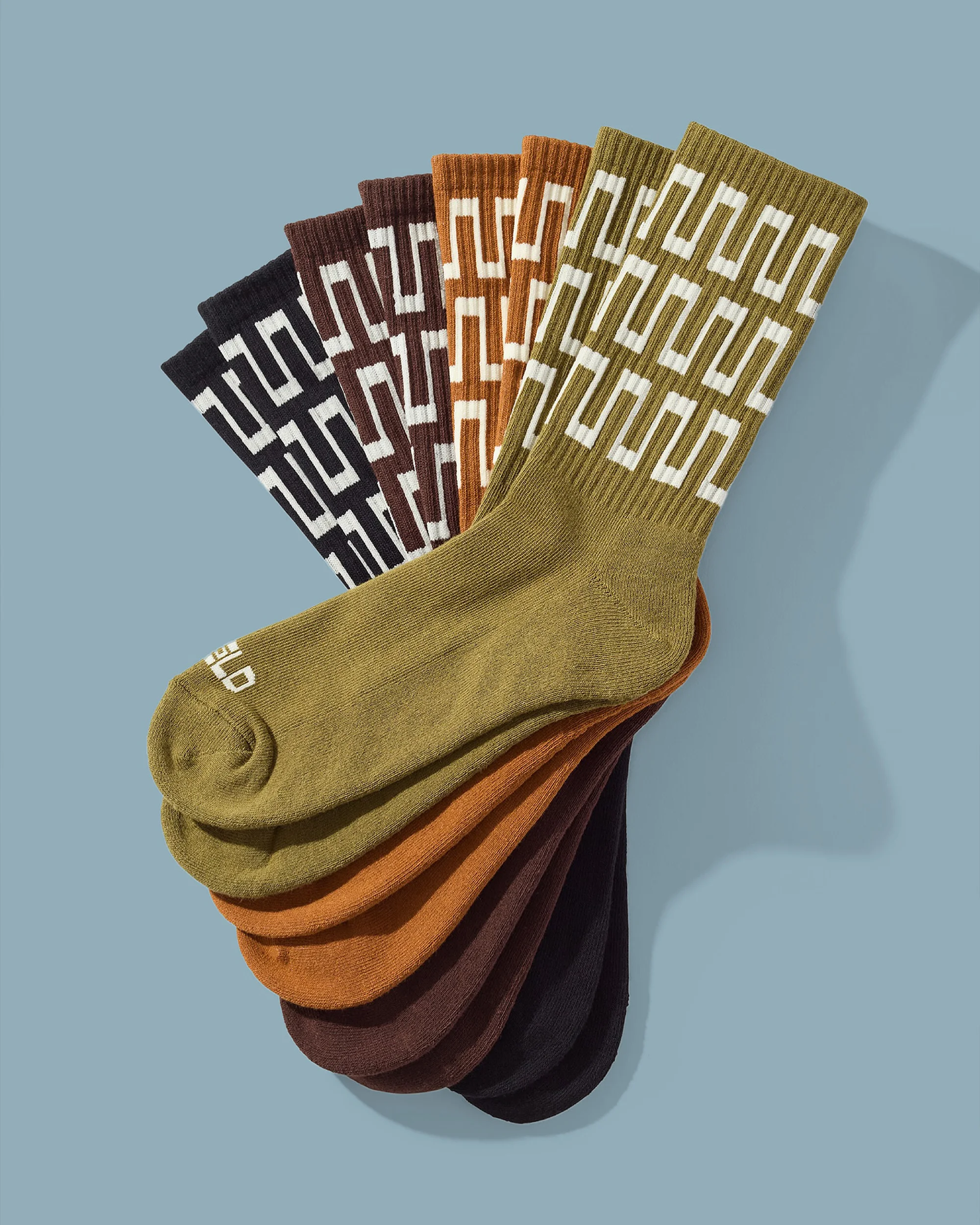 Several olive green, brown, and black patterned socks are arranged on a blue surface in a retail or studio product shot.