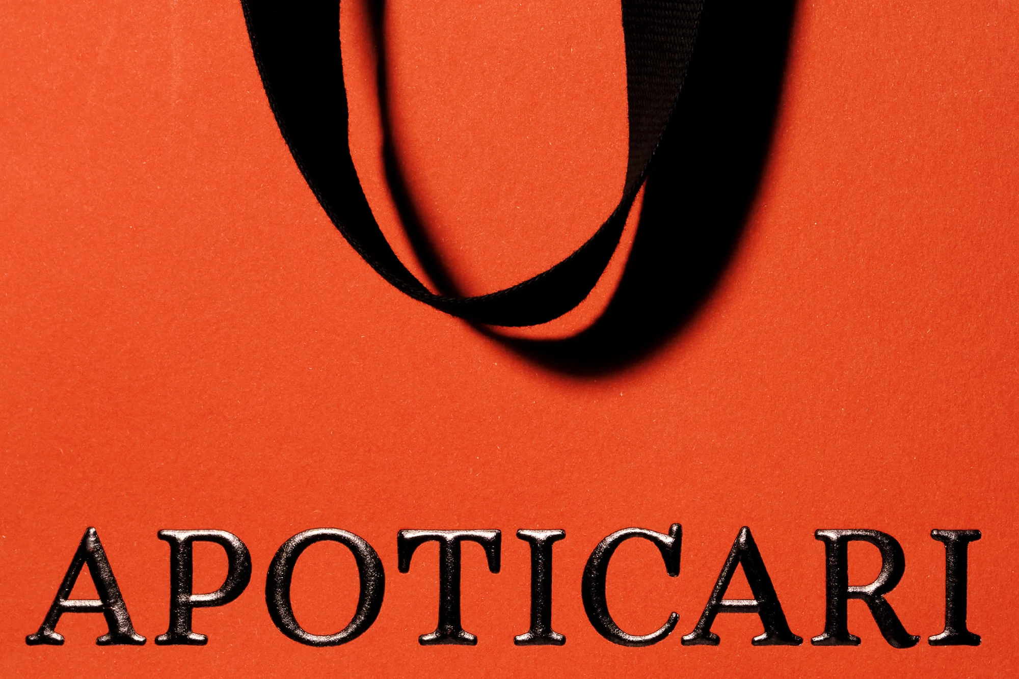 Close-up of an orange shopping bag featuring black straps and the dark grey text 'APOTICARI' at the bottom of the image.