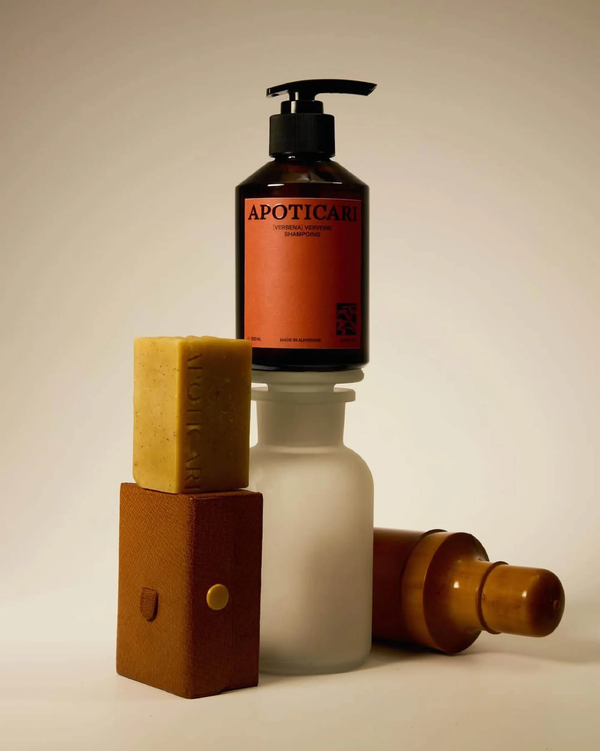 Amber glass shampoo bottle with pump on top of a stack of soap, containers, and bottles in a minimalist skincare product shot.