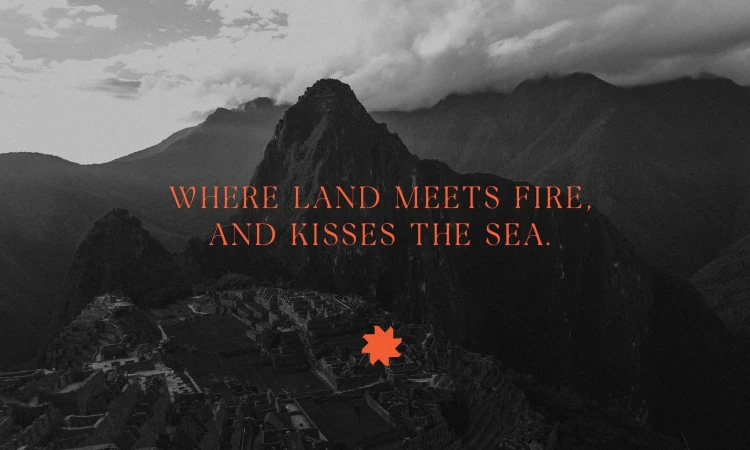 High-angle view of Machu Picchu ruins in Peru surrounded by mountains with text overlay saying, 'Where land meets fire, and kisses the sea.'