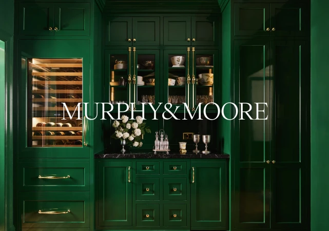 Elegant green kitchen with custom cabinetry, marble countertop, wine storage, and decorative dishware and barware.