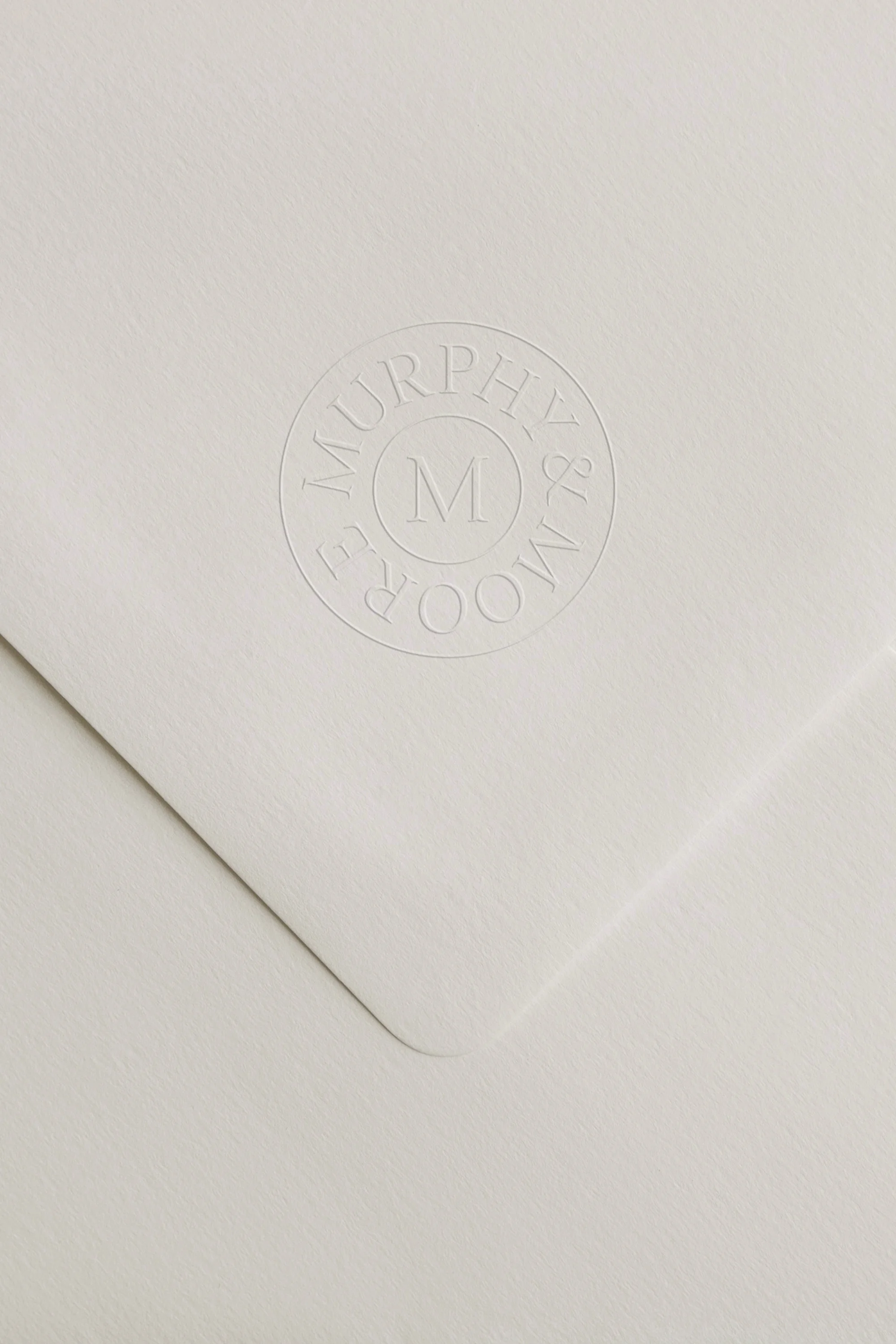 Close-up of a white envelope with a debossed round logo reading 'MURPHY & MOORE' and a large 'M' in the center.