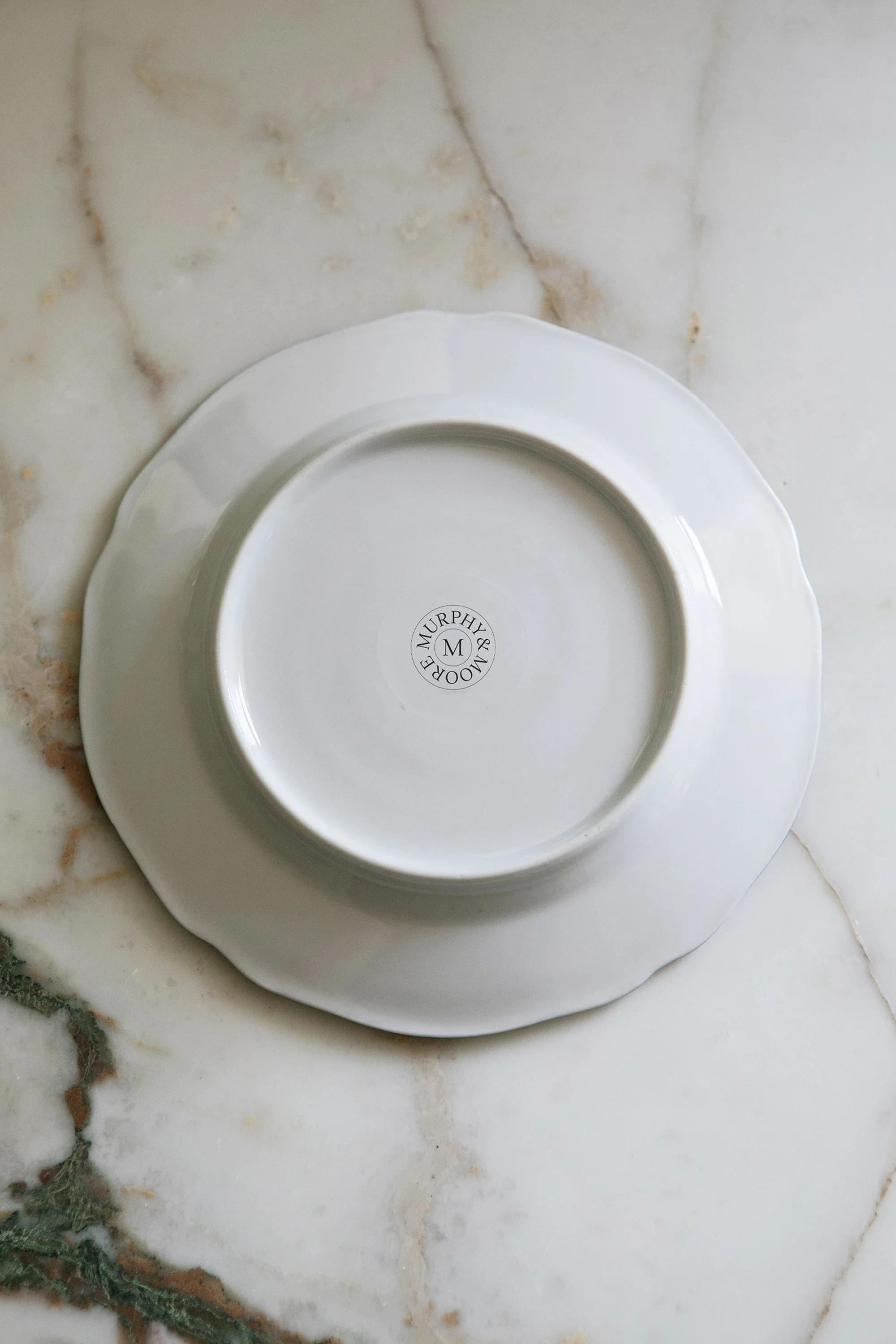 Overhead shot of a round, white plate with a scalloped edge, placed on a marble surface, featuring the 'Murphy's Moore Good Food' logo.