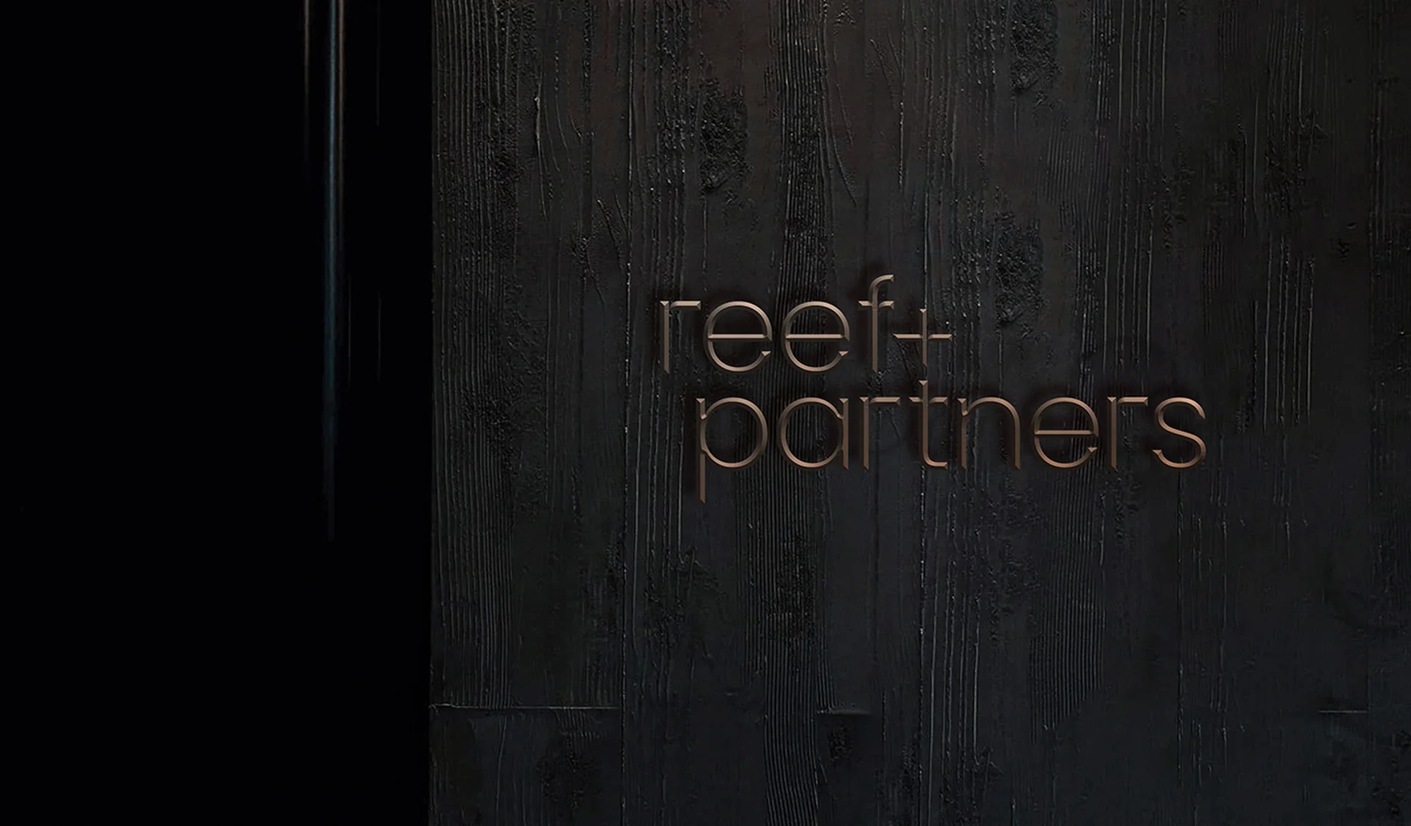 Elegant dark wooden wall with the 'reef+partners' logo in gold lettering creates a sophisticated and professional ambiance.