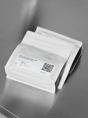 Two white sealed coffee bags sit at an angle on a reflective metal surface, showcasing minimalist design and product presentation.