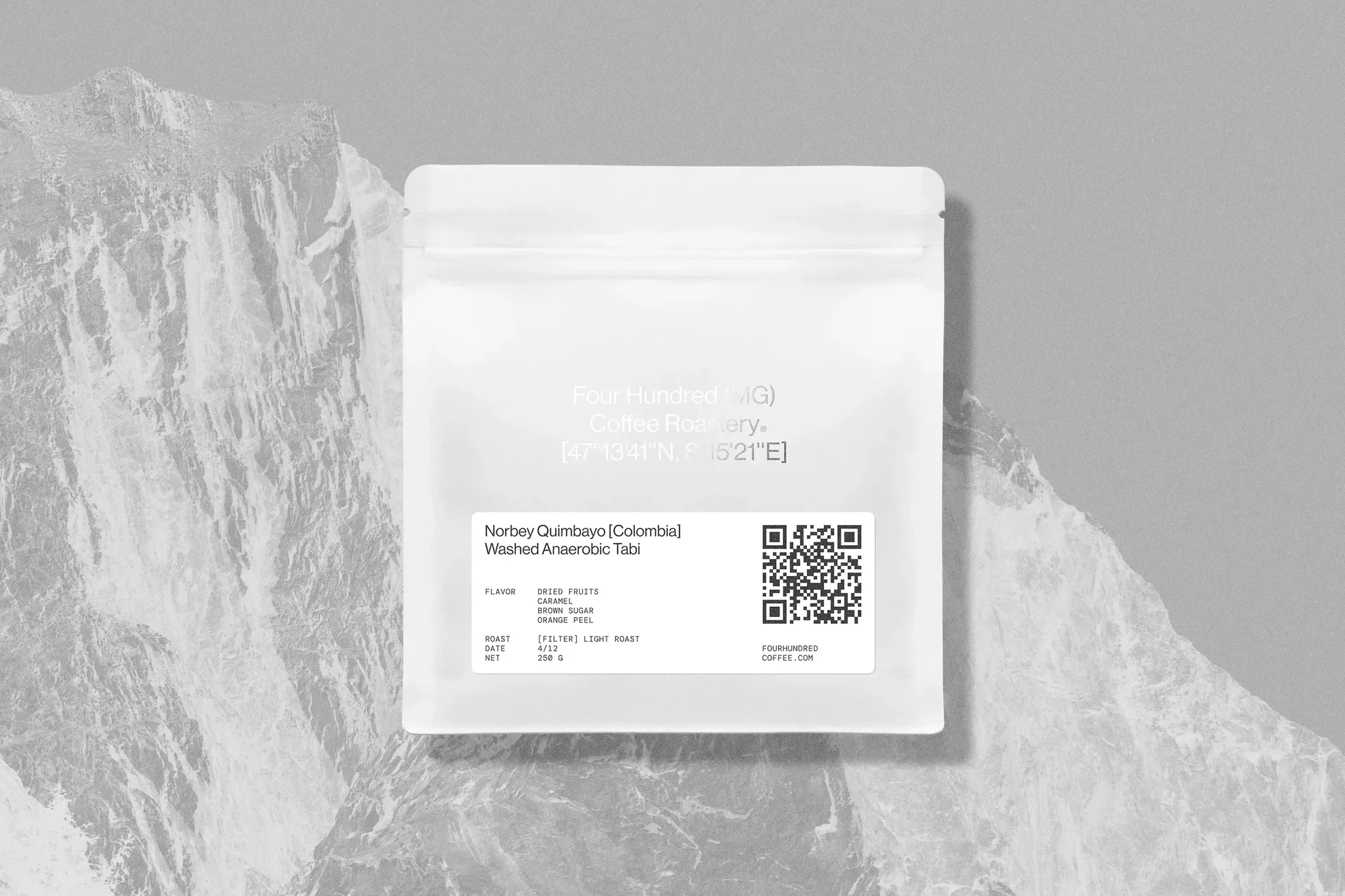 A white bag of Four Hundred MG coffee sits against a textured gray mountain backdrop, creating a minimalist, high-contrast product shot.