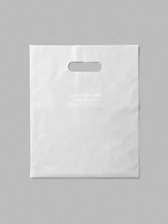 Isolated white plastic shopping bag with cutout handles on a gray surface, featuring a coffee roastery logo and branding text.