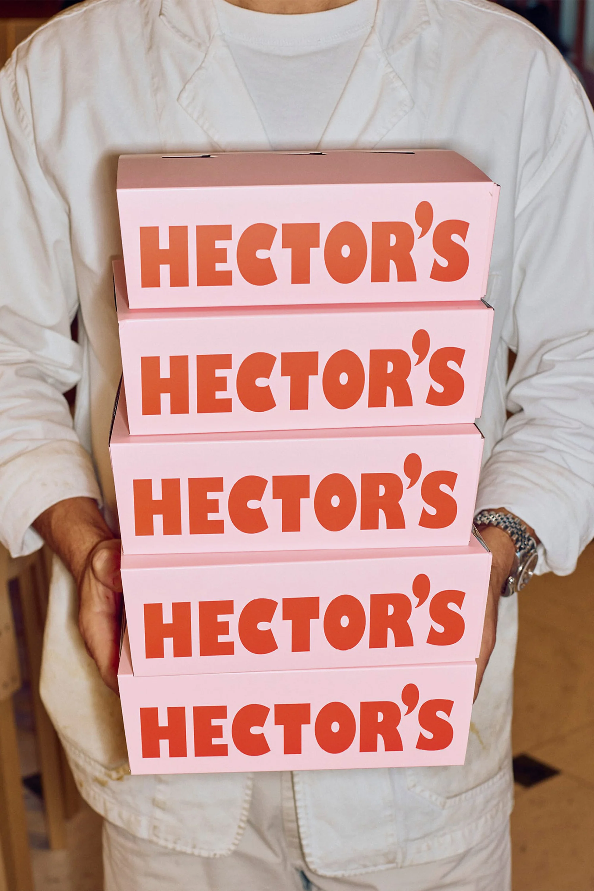 A person holds a stack of pink Hector's boxes with red lettering, showcasing the brand and focus on food presentation and service.