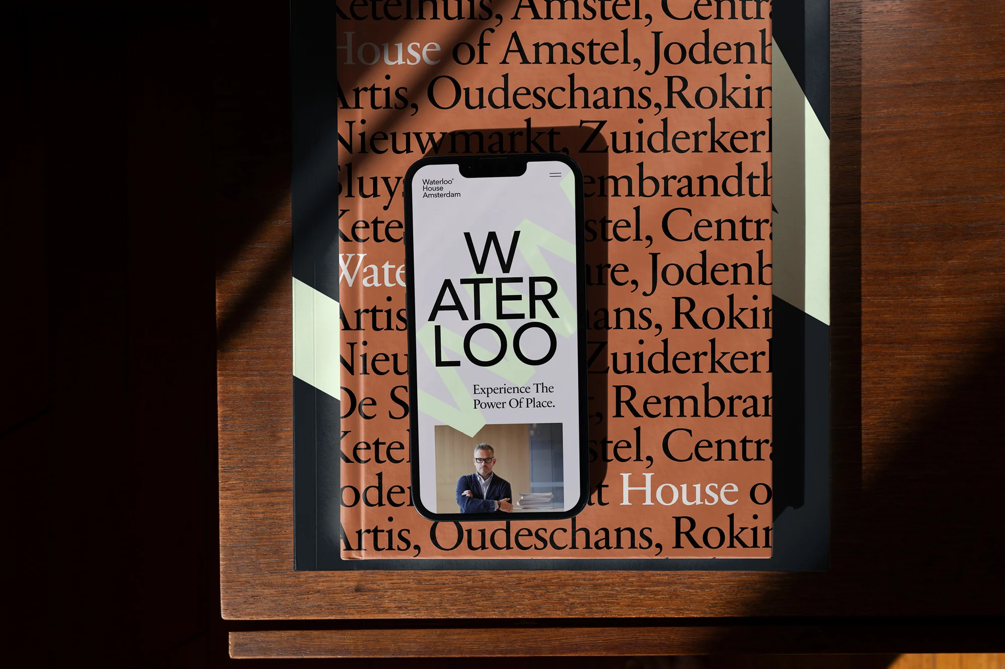 Smartphone displaying Waterloo House website, placed on a book with similar typography, creating a harmonious design and promoting visual appeal.