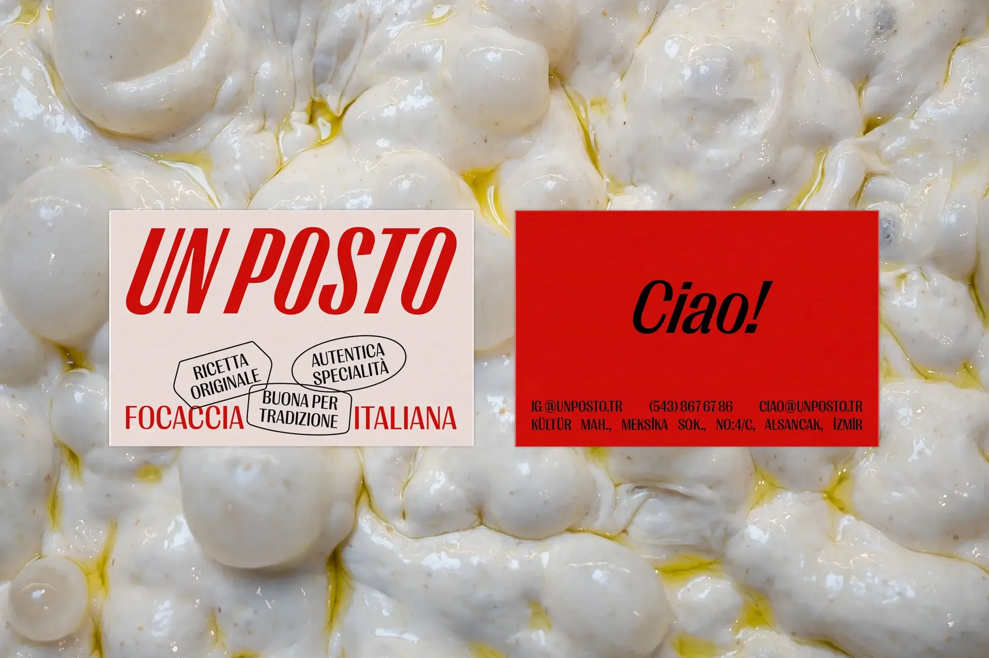 Close-up of focaccia dough with visible olive oil, alongside red and beige signs displaying brand name and Italian descriptions.