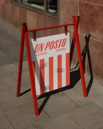 A red A-frame sandwich board sign advertises "Un Posto Focaccia Italiana" with red and white stripes, sitting on a paved surface.