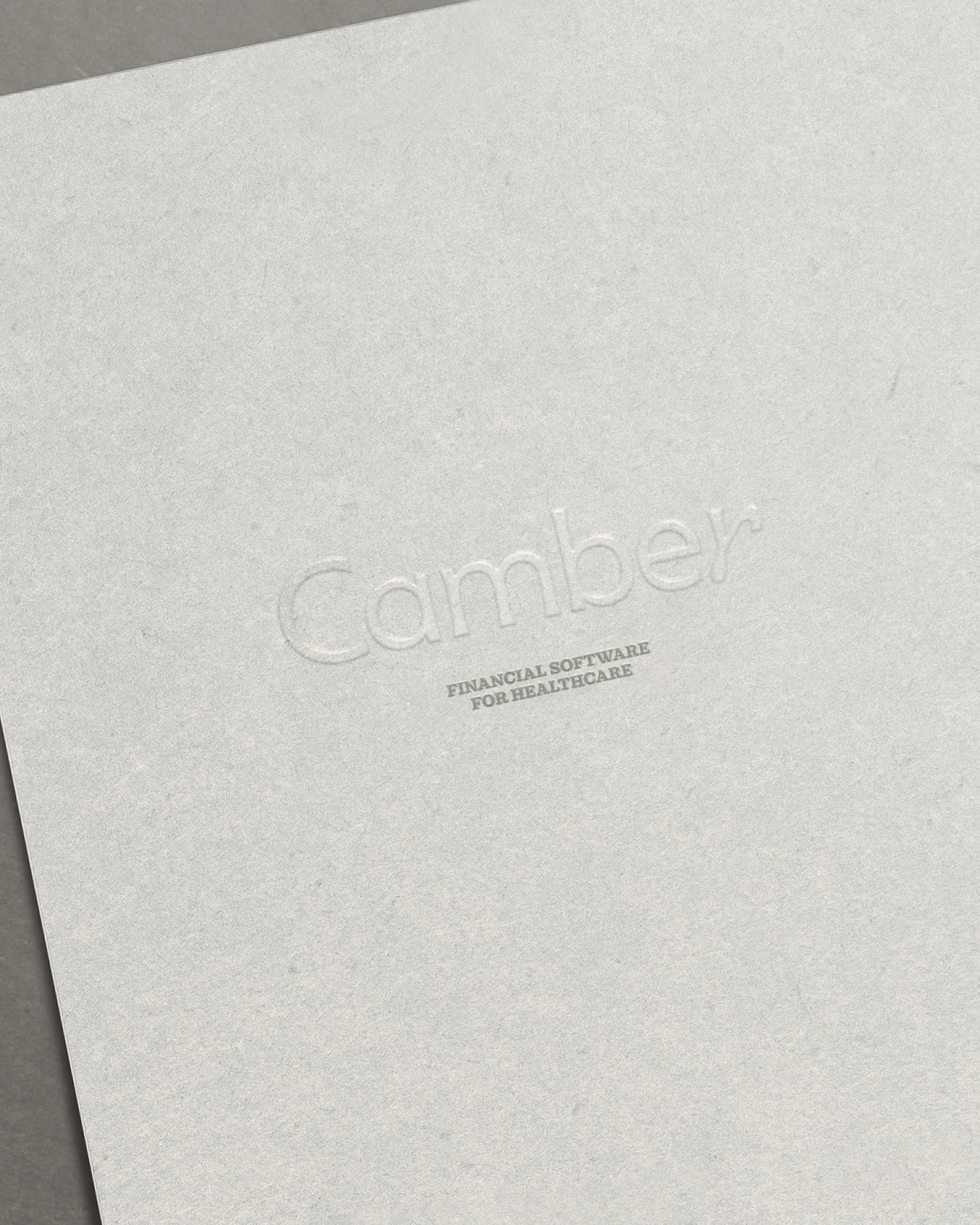 Close-up of textured paper with the embossed logo and text for Camber Financial Software for Healthcare in a minimalist style.