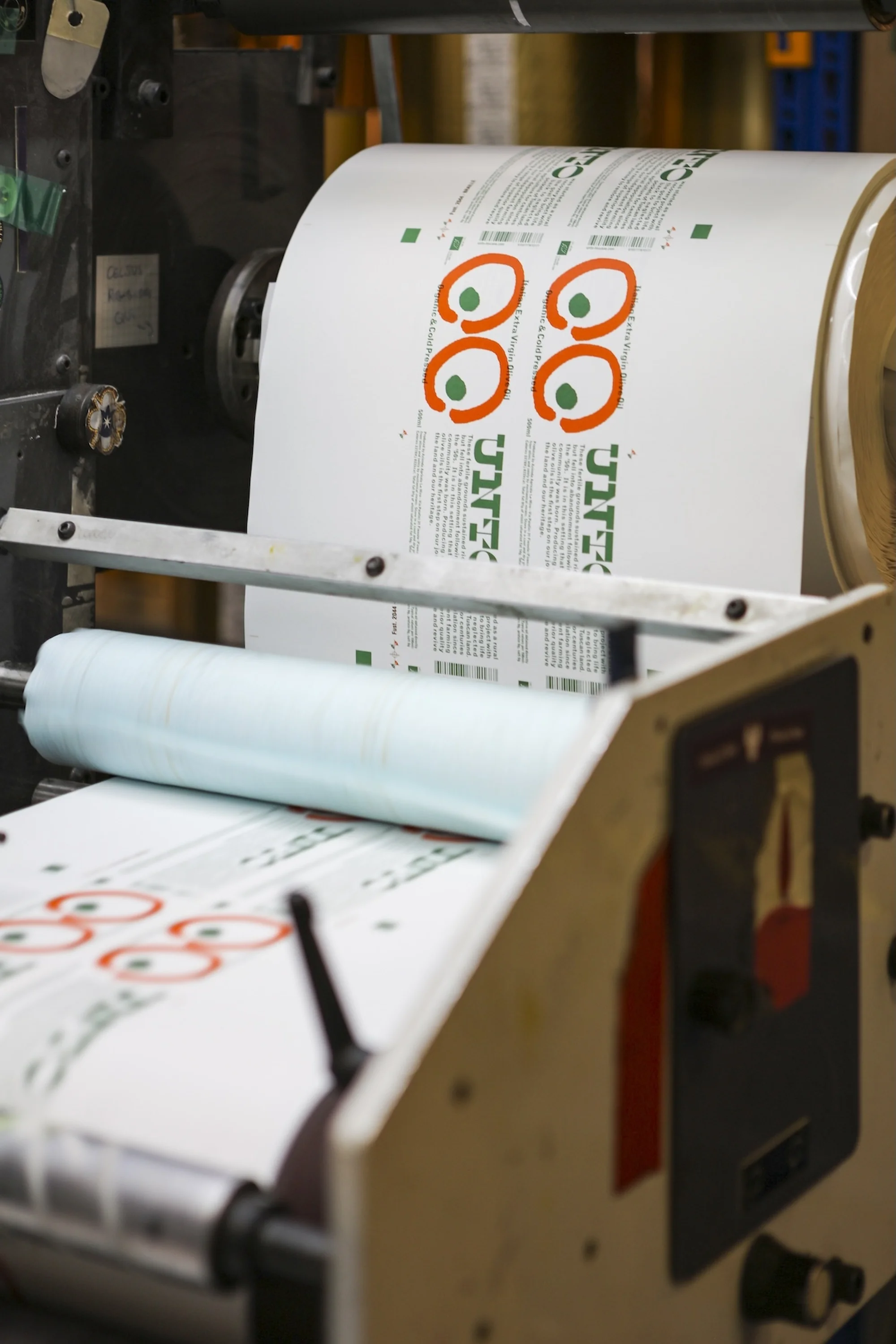 Printing press with a roll of printed labels featuring an eye-catching design with orange circles and green accents, processed on machinery.