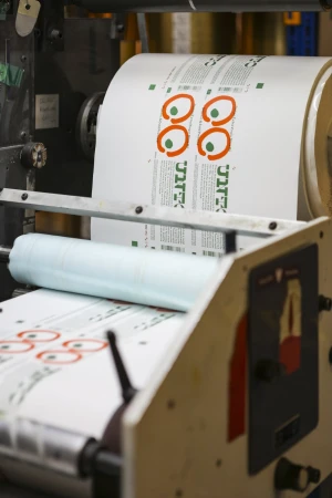 Printing press with a roll of printed labels featuring an eye-catching design with orange circles and green accents, processed on machinery.