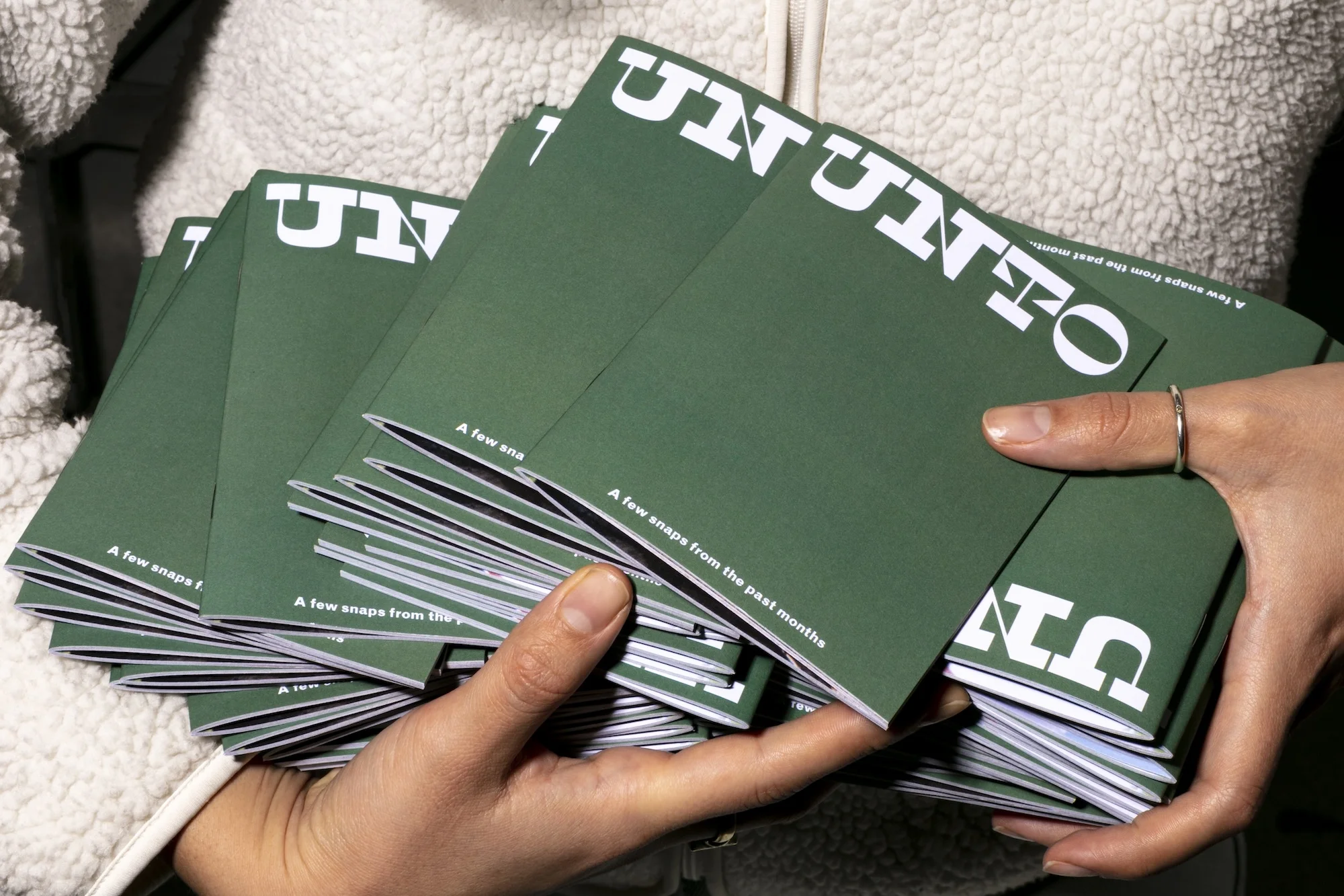 Close-up on a person holding a stack of green booklets with the word 'UUTTO' printed in white text on each cover.