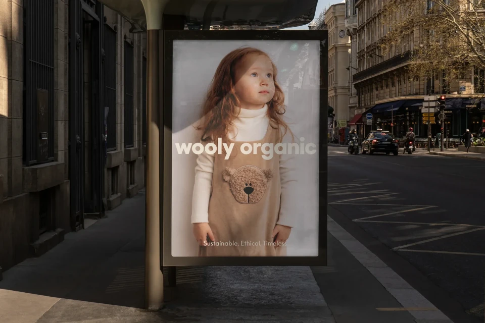 Outdoor advertisement featuring a young red-haired child in a dress with a bear on it, displayed on a city street in Europe.