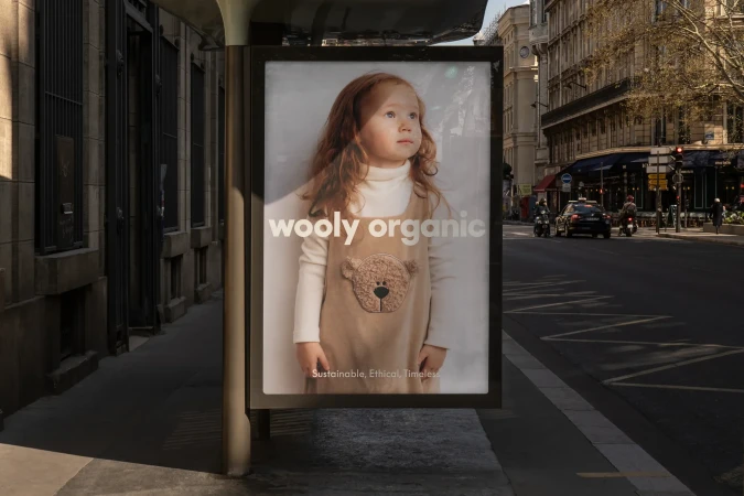 Outdoor advertisement featuring a young red-haired child in a dress with a bear on it, displayed on a city street in Europe.