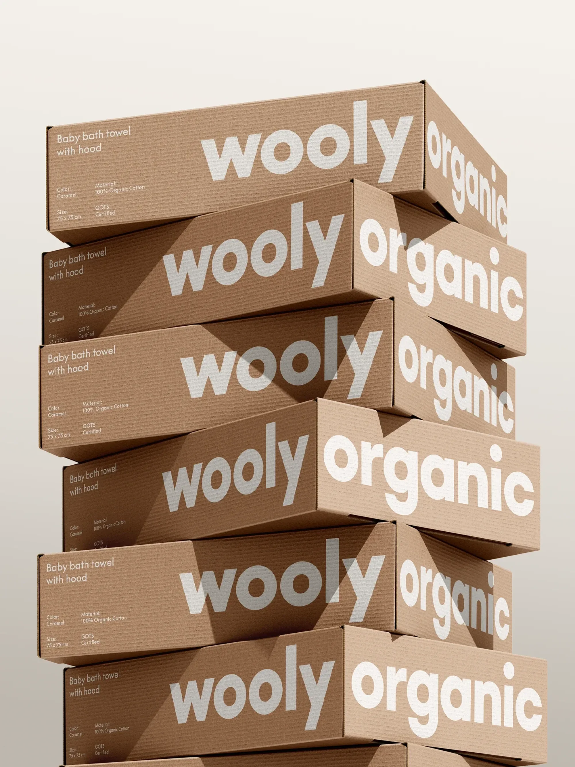 Stacked packaging boxes of Wooly Organic baby bath towels with hood. Tan cardboard boxes with white logos and product descriptions.