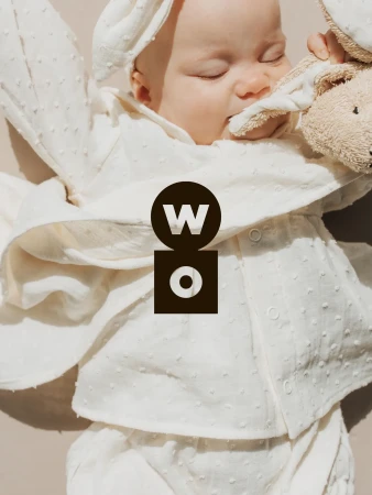 Baby sleeping in white textured clothing holding a plush toy for Wooly Organic