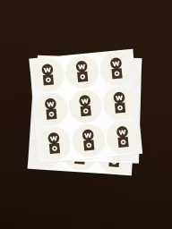 Stacked sheets of circular round sticker labels featuring brand logos placed on a dark surface.