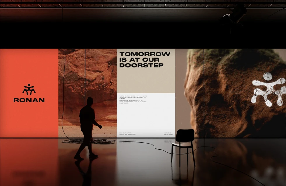 Person walking across a reflective floor past large displays with brand logos, landscape images, and typographic text in a gallery setting.