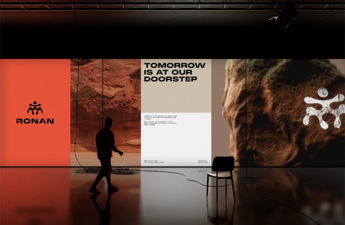 Person walking across a reflective floor past large displays with brand logos, landscape images, and typographic text in a gallery setting.