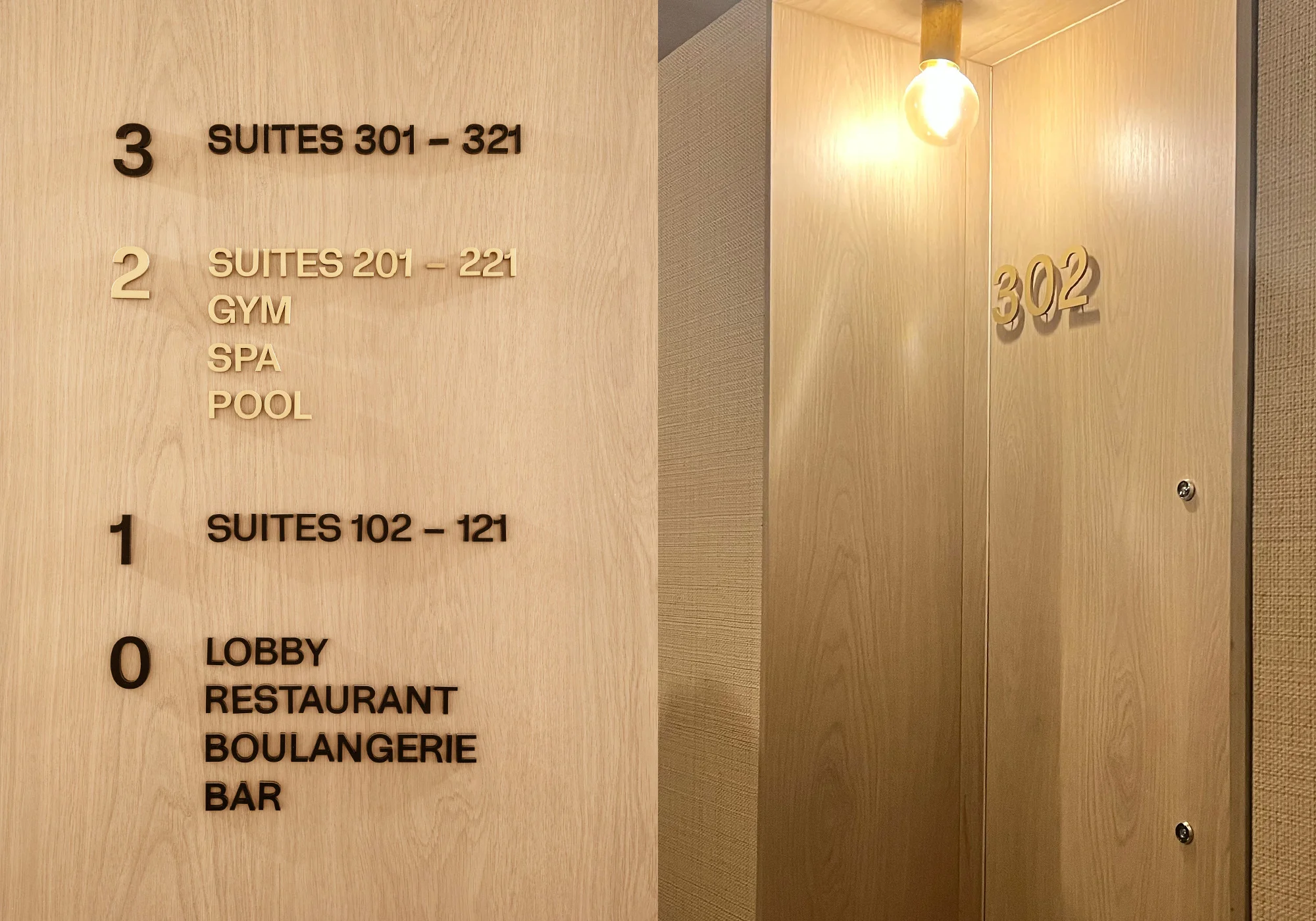 Hotel signage displays floor numbers and services: suites, gym, spa, pool, lobby, restaurant, boulangerie, and bar, lit by a bulb.