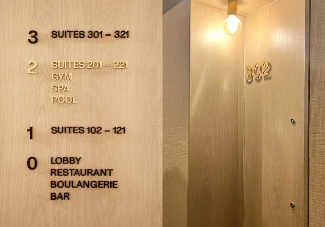 Hotel signage displays floor numbers and services: suites, gym, spa, pool, lobby, restaurant, boulangerie, and bar, lit by a bulb.