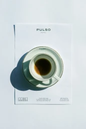 Overhead shot of a white coffee cup and saucer resting on branded hotel stationery under direct natural light.