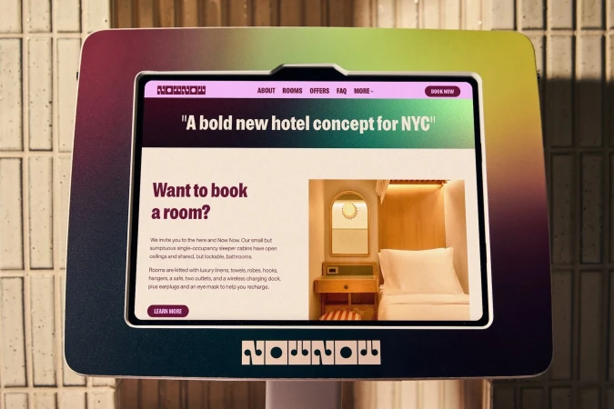 Promotional display showing a hotel room interior on a digital screen; the advertisement features travel and modern living concepts.