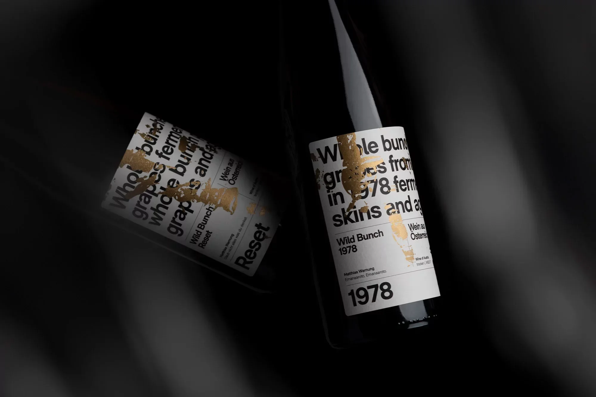 Two wine bottles with white labels and gold accents are positioned against a dark background, creating an elegant and minimalist still life.