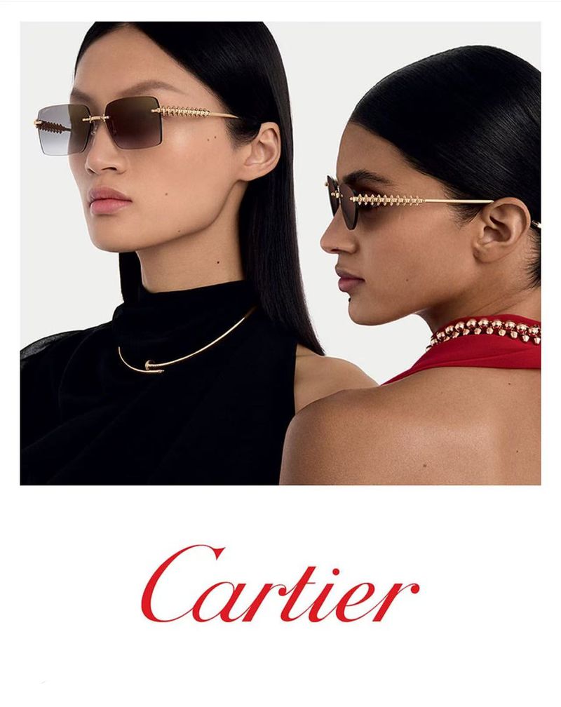 Two women wearing sunglasses and jewelry in a beauty product ad. The ad features a red Cartier logo on a white background.