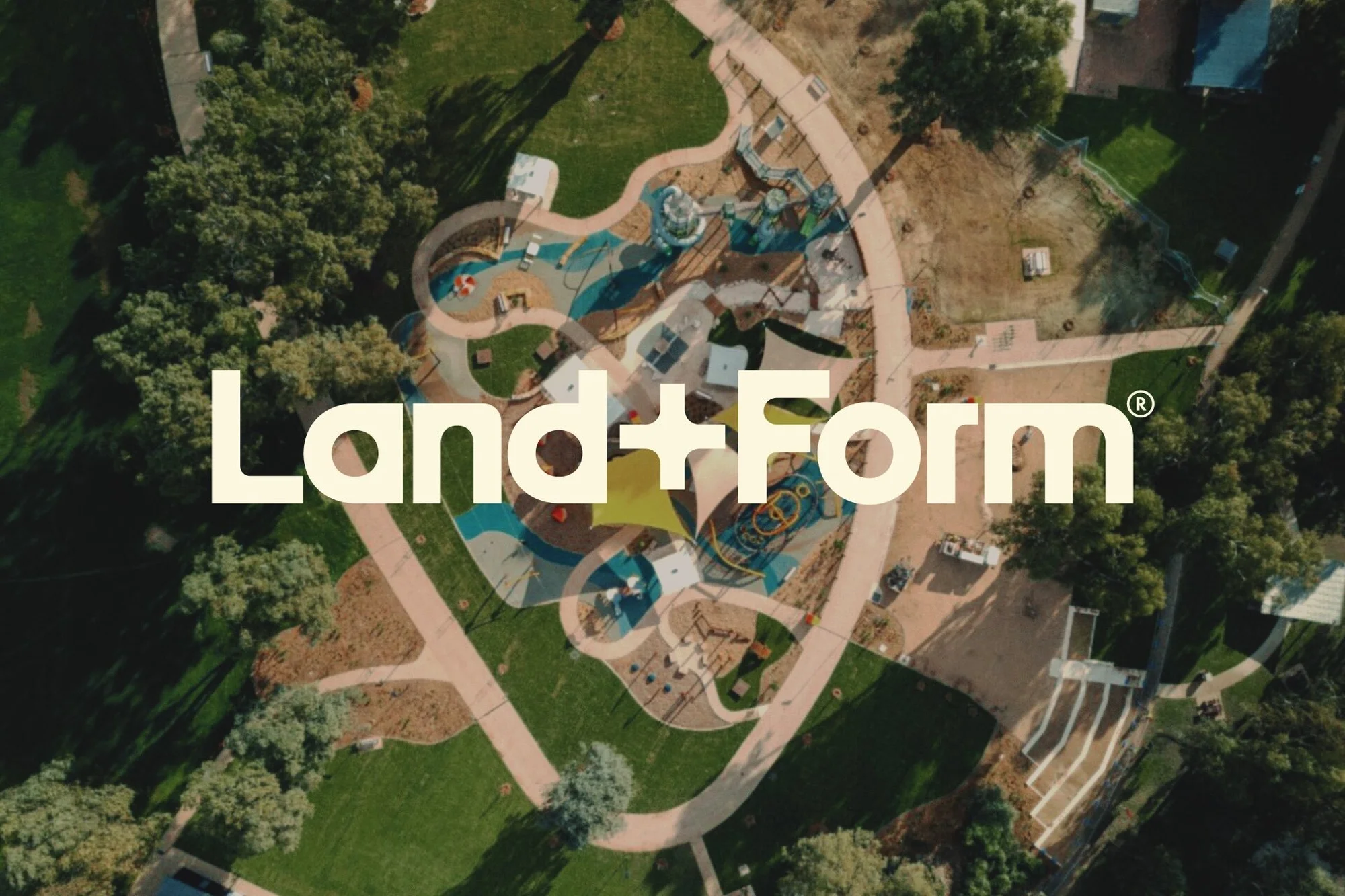 Aerial view of a park featuring walking paths and a playground, with the Land+Form logo overlayed, showcasing landscape architecture.