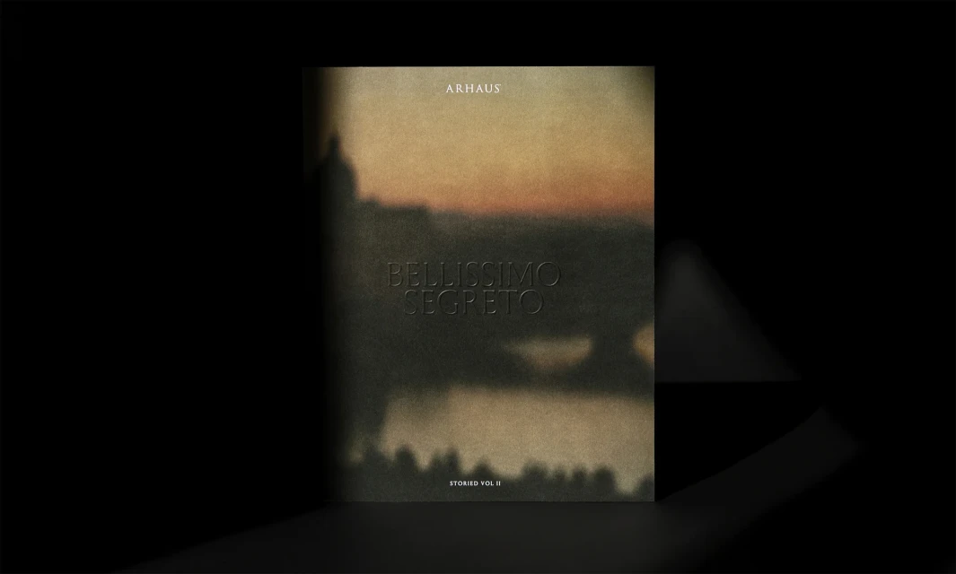 Art book cover featuring blurred landscape and the title "Bellissimo Segreto Stories Vol II" by Arhaus against a dark backdrop.
