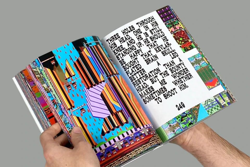 Open book displays colorful abstract art and black text, held open by two hands against a neutral gray backdrop in a close-up shot.