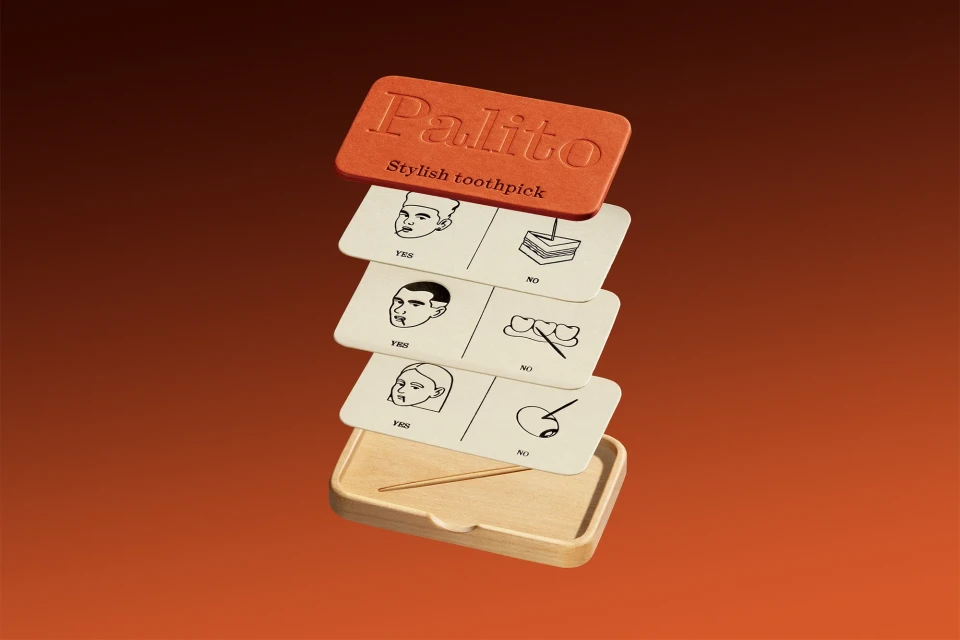 Elevated view of an orange Palito toothpick dispenser, cards with line drawings, and a wooden holder on an orange gradient backdrop.