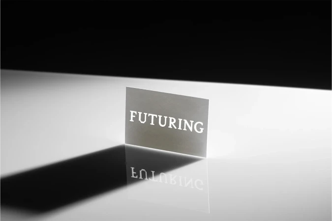 Abstract studio shot of a backlit card with the text 'FUTURING' cut out, casting a sharp shadow and reflection on a glossy surface.