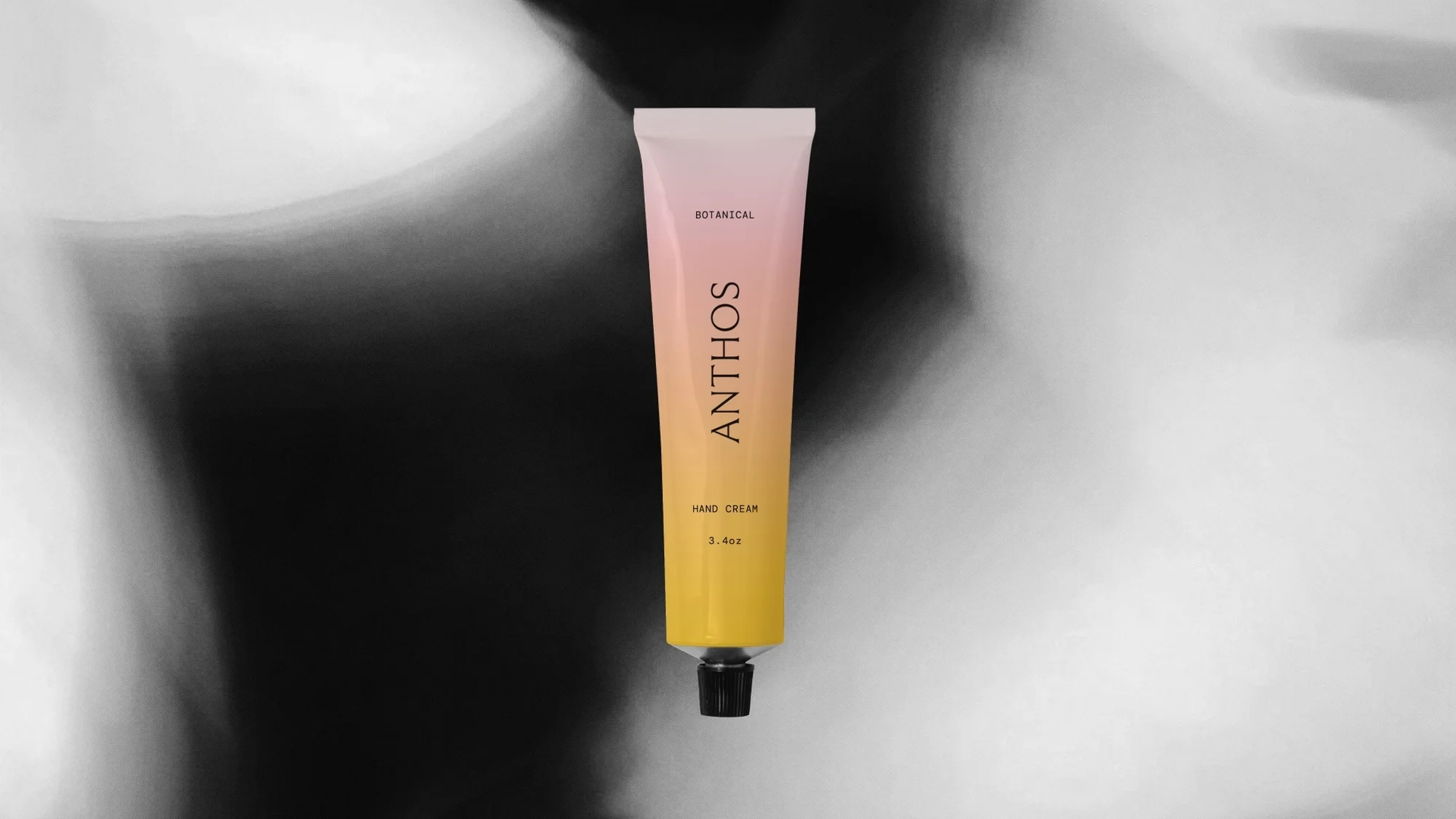 Anthos hand cream tube with a pink-to-yellow gradient, product shot against blurred grey background, close-up studio product photography.