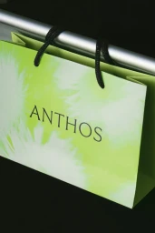 Light green Anthos shopping bag with black rope handles hanging on a silver metal bar
