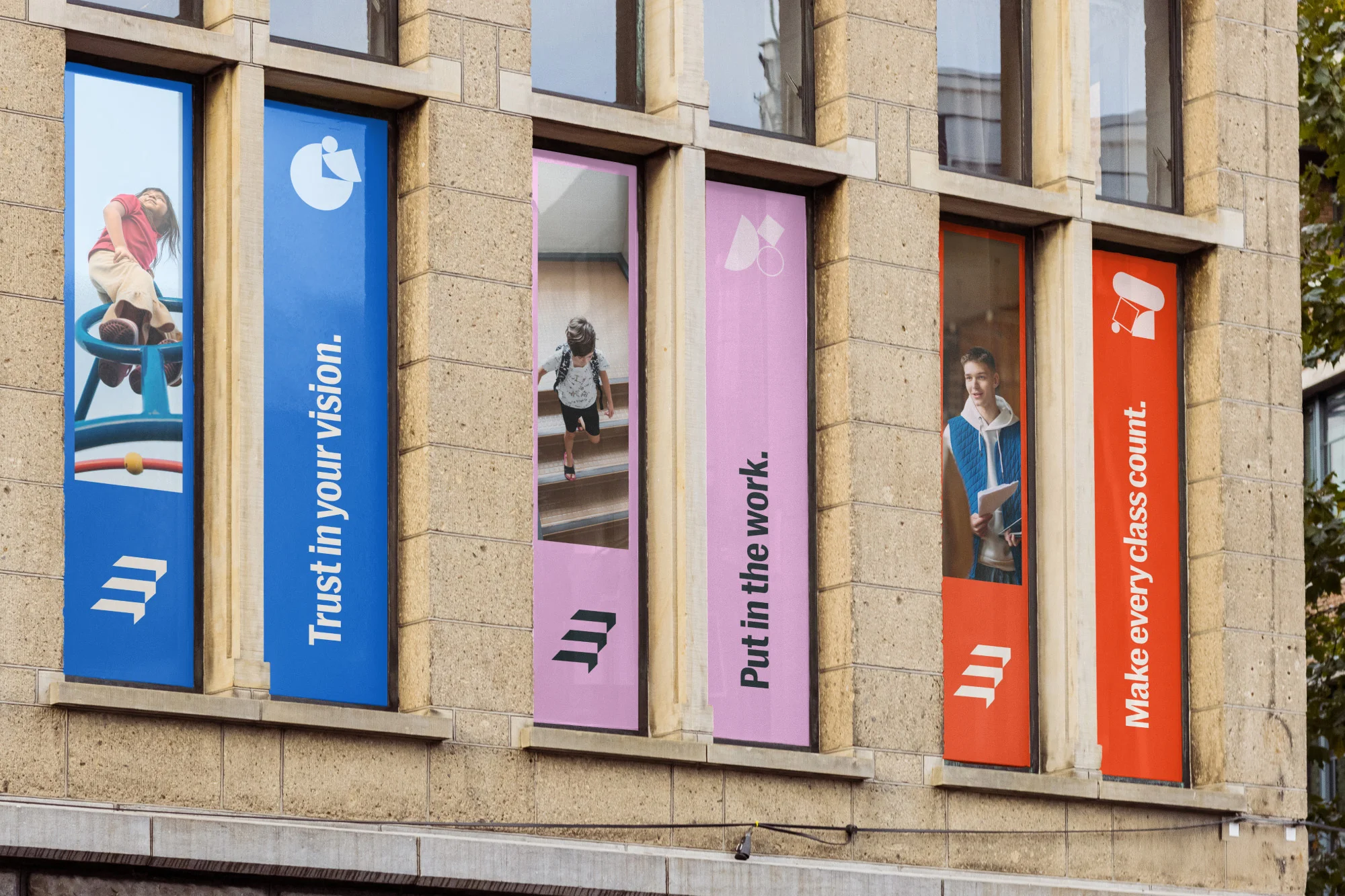 Building facade featuring banners in windows showcasing children and educational slogans like 'Trust in your vision'.