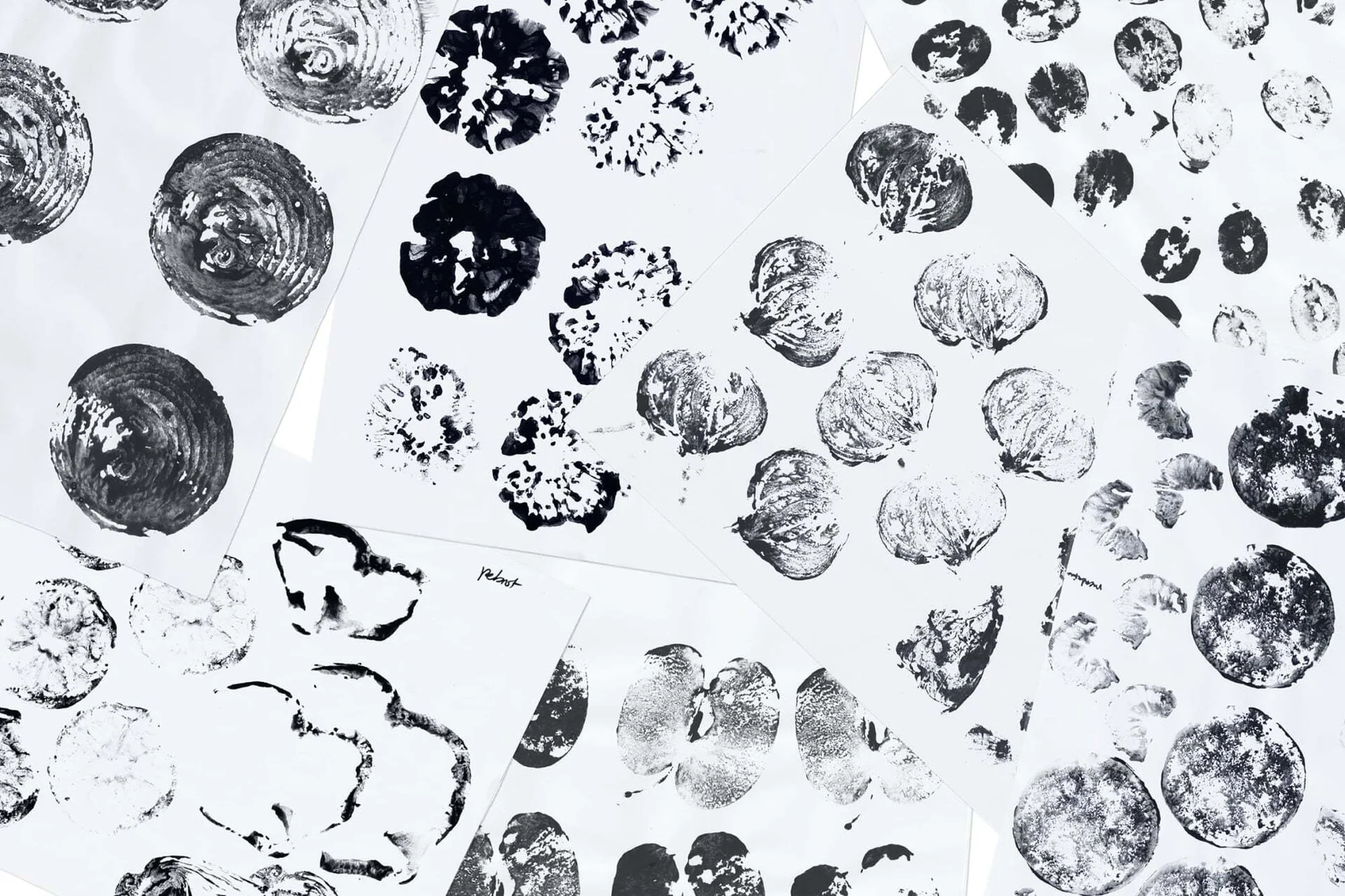 Collection of monochrome ink-stamped patterns on white paper; circular and abstract botanical shapes create an artistic composition.
