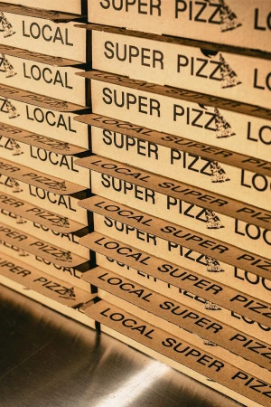 Stack of cardboard pizza boxes labeled 'Local Super Pizza' in a vertical shot, suitable for food and restaurant marketing.