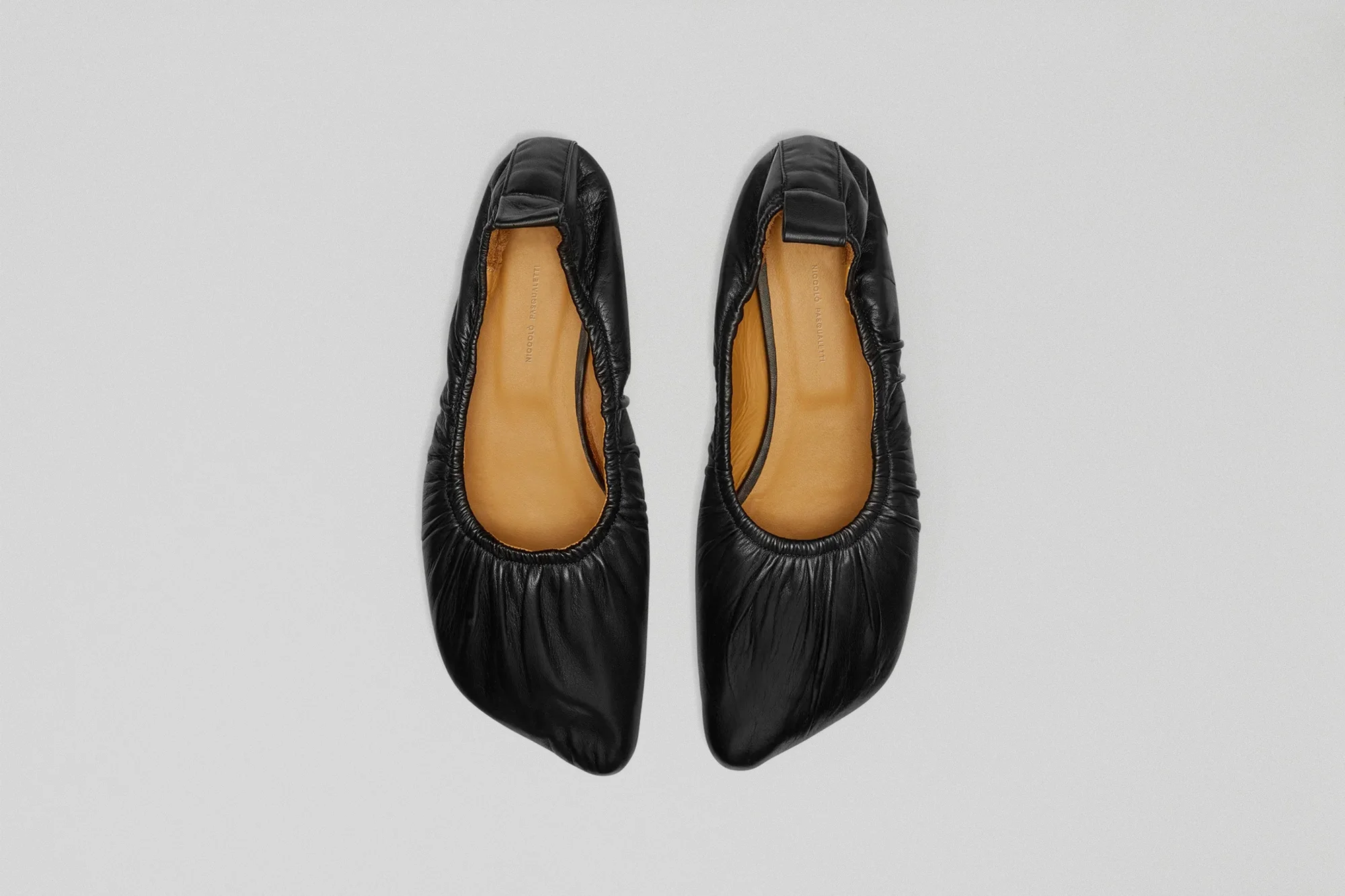 Elevated view of black leather ballet flats with a light tan interior lining against a white background, showcasing fashion footwear.
