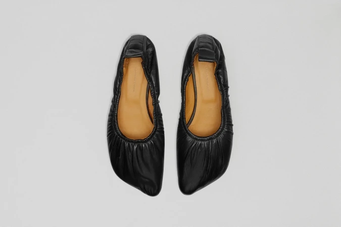 Elevated view of black leather ballet flats with a light tan interior lining against a white background, showcasing fashion footwear.