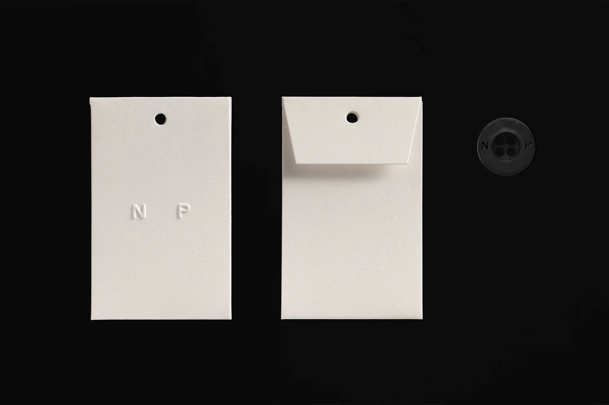 Close-up studio shot of two white tags and a round button with letters on a black background, featuring clean design and minimalist style.