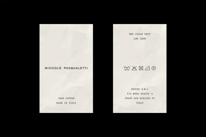 Two cream clothing labels with black typewriter text on a black background