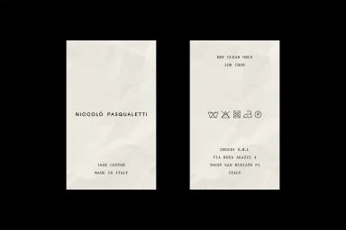 Two cream clothing labels with black typewriter text on a black background