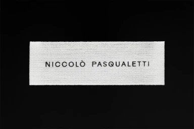 White woven clothing label featuring black typography centered on a solid dark background.