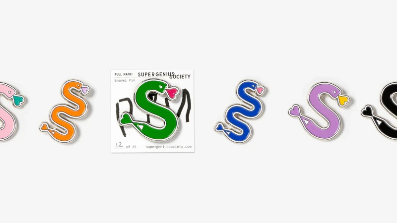 Several enamel pins with silver borders shaped like an 'S' that resembles a snake are lined up against a white background. Various colors.