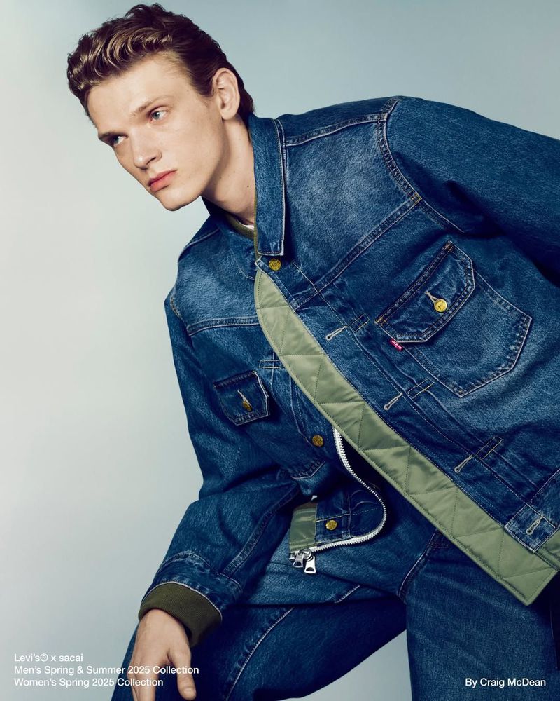 Fashion editorial of a young adult male model wearing a denim jacket and jeans against a neutral backdrop. The image showcases the clothing texture.